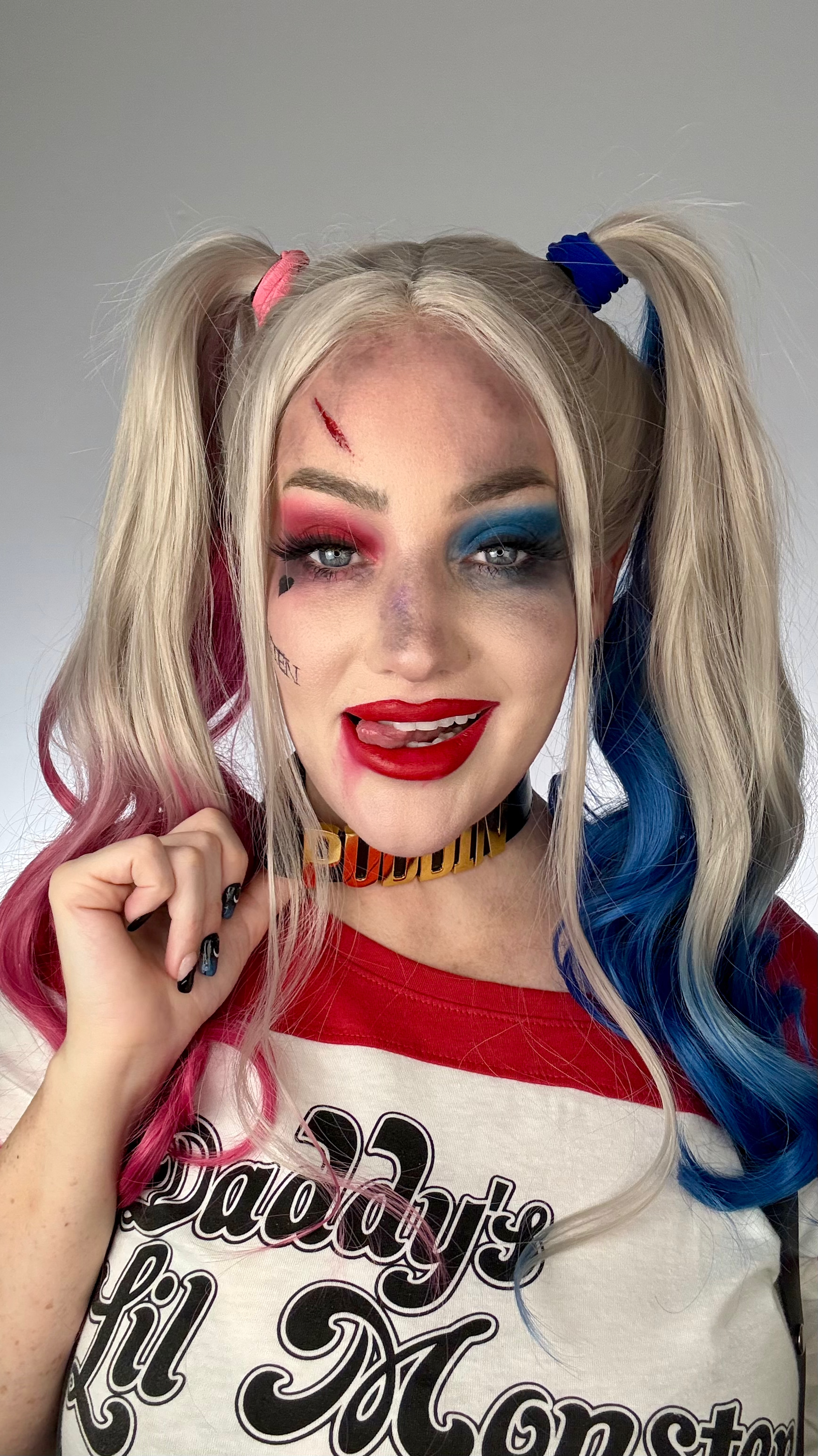 Playful Harley Quinn Halloween cosplay pose showing pink and blue pigtail wig and outfit.